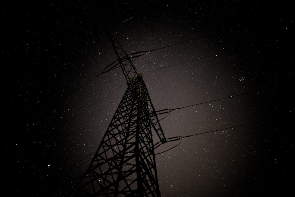 Ein Sternenhimmel bei Nacht, im Vordergrund ein Hochspannungsmast