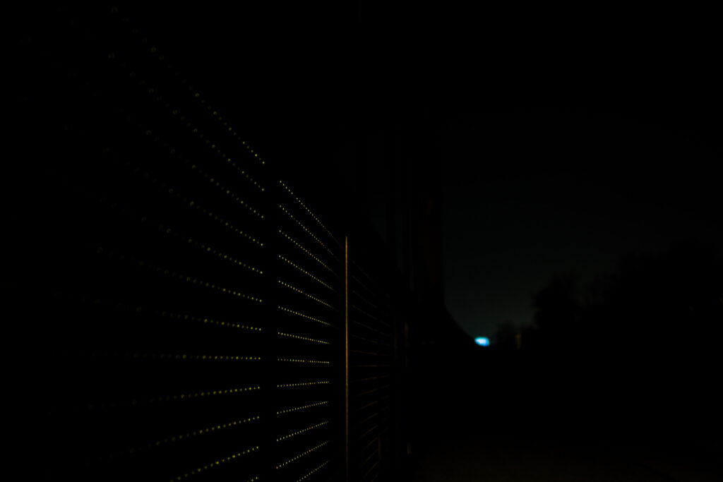 Ein Geländer bei Nacht, Ein Lochblech als Seite, durch die Löcher fällt auffällig viel Licht, ein surrealer Eindruck entsteht.